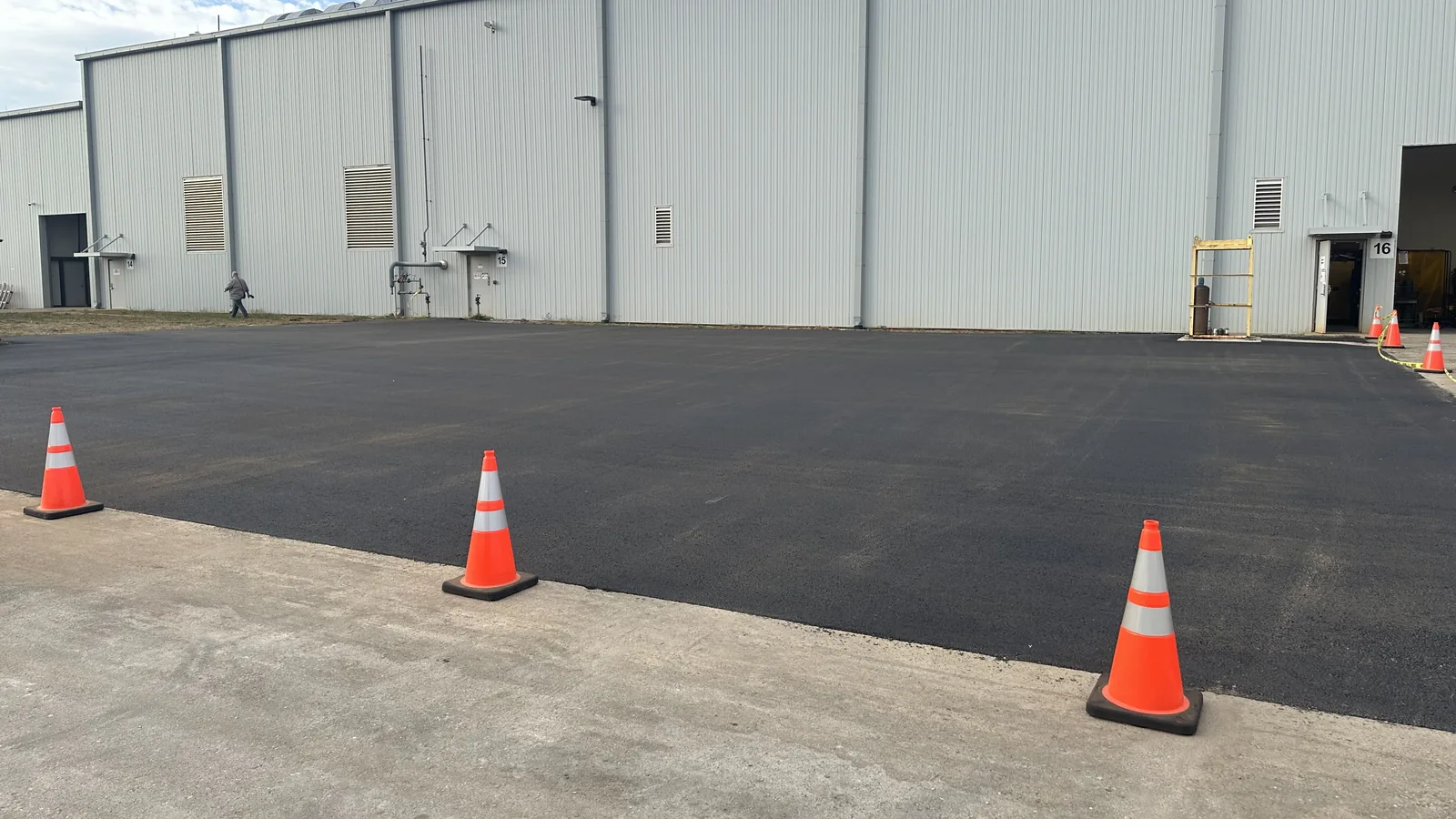 Paver and dump truck laying asphalt beside an industrial building, asphalt paving