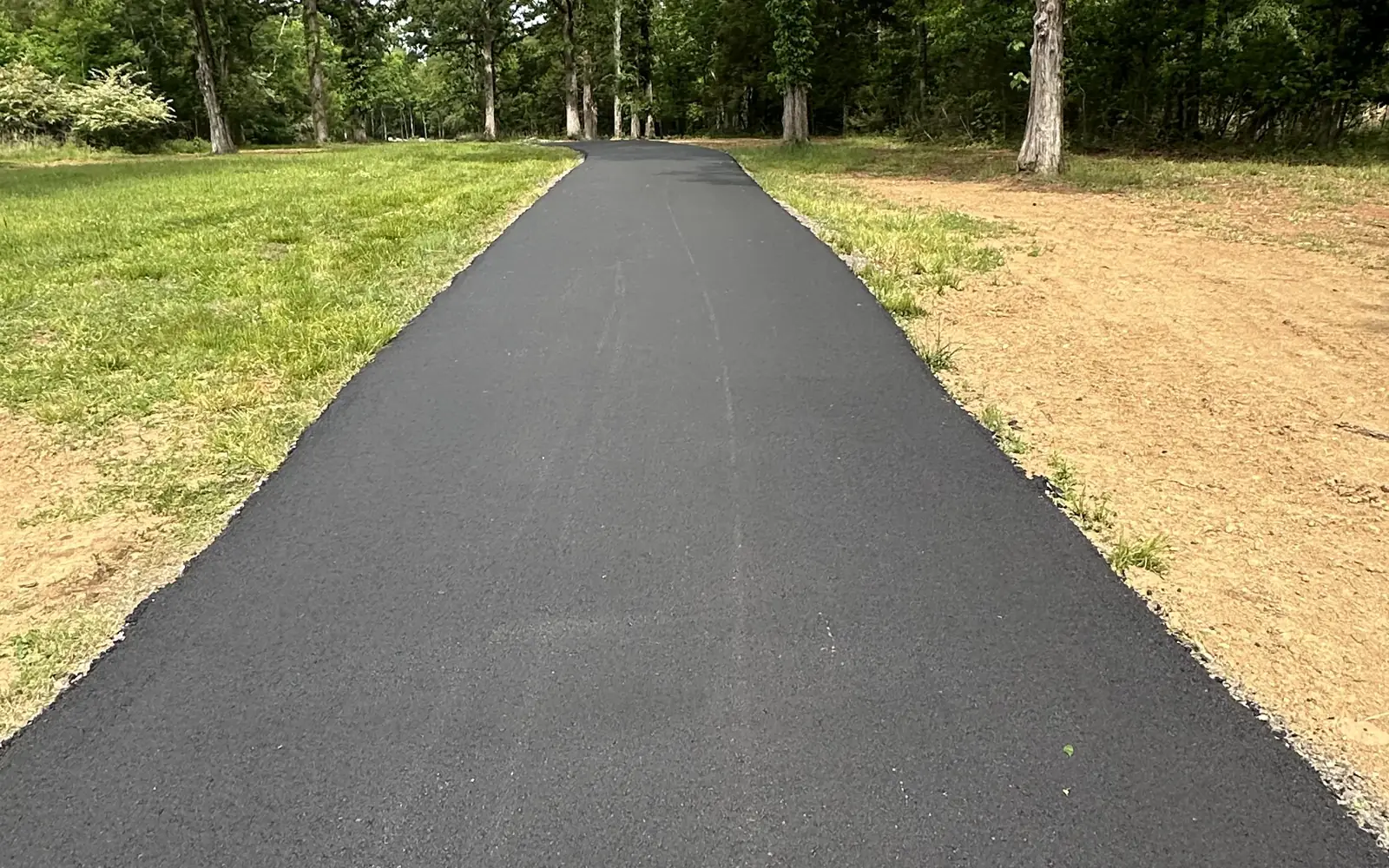 Finished asphalt driveway curving through a wooded lot, asphalt driveway paving