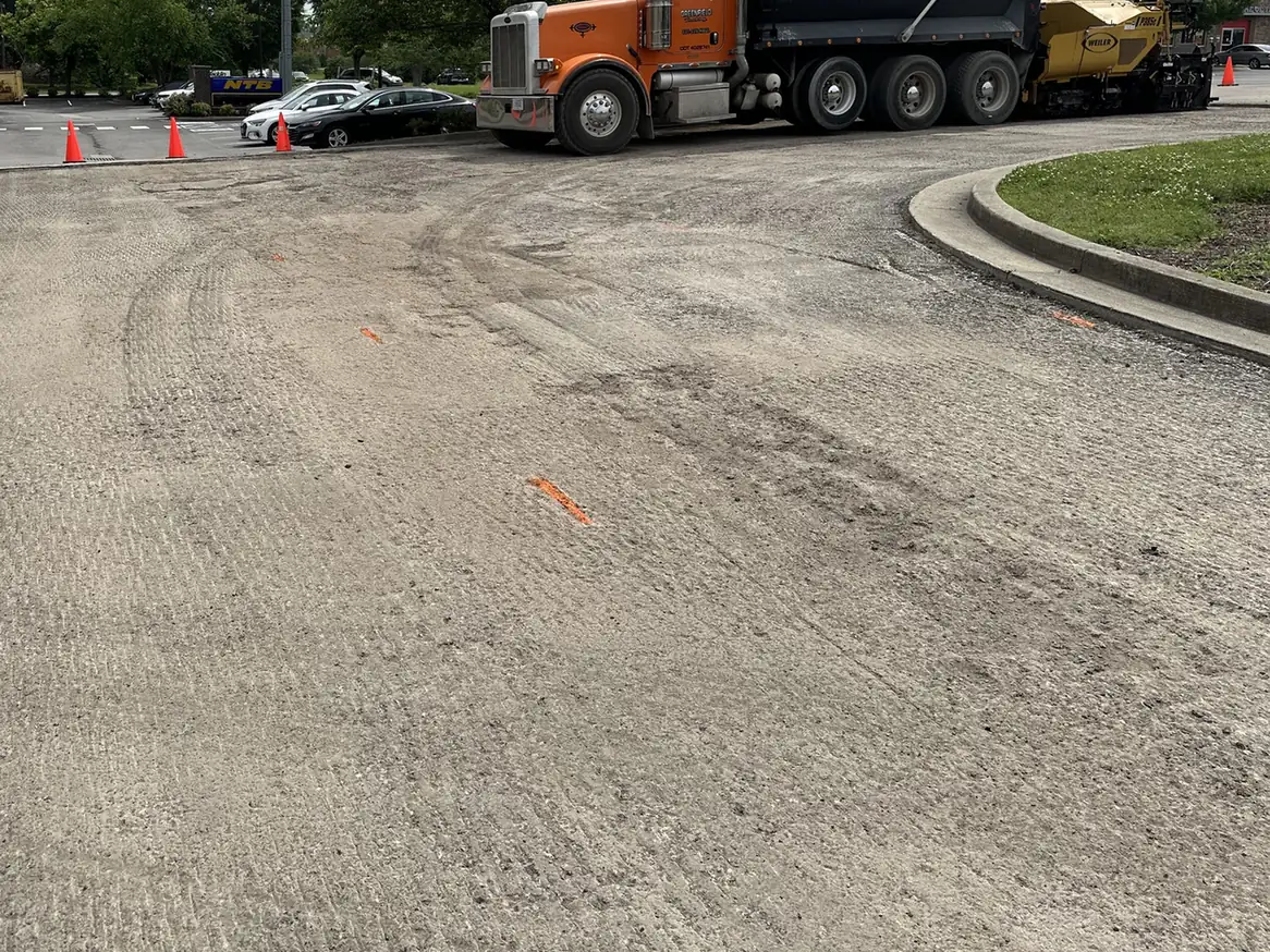Milled parking lot surface with a dump truck and paver at the far end, asphalt milling