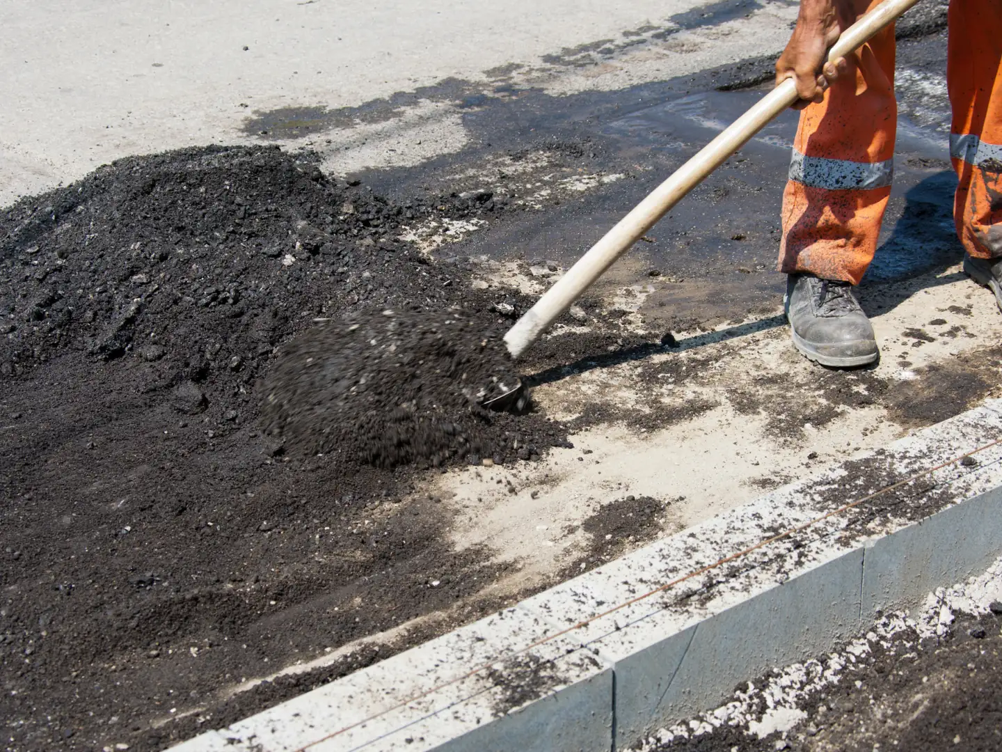 Pile of asphalt millings being raked beside a curb, asphalt milling