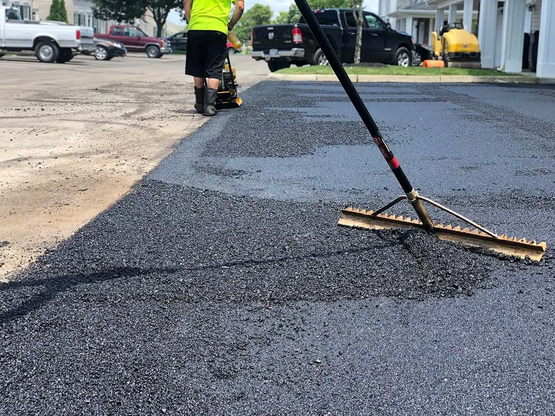 Fresh asphalt patch on a driveway being raked smooth, asphalt repair