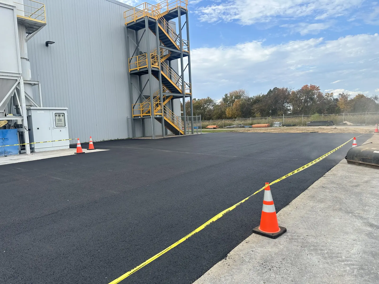 New asphalt section paved and coned off beside an industrial building, asphalt repair