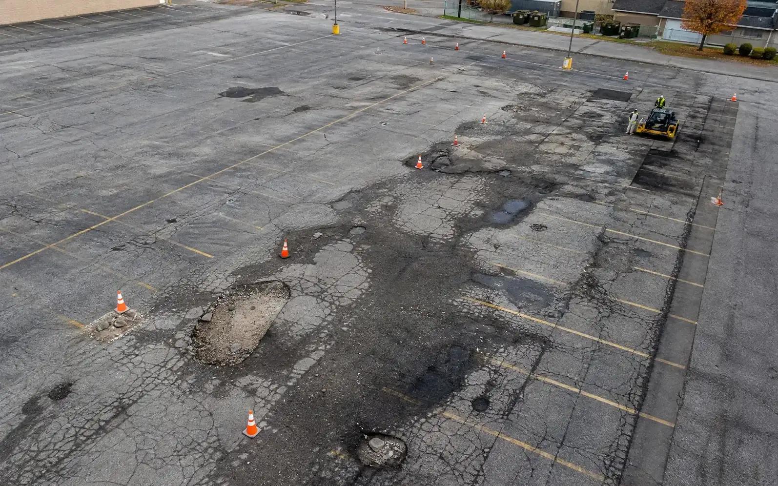 Cracked parking lot with potholes coned off before patching, asphalt repair