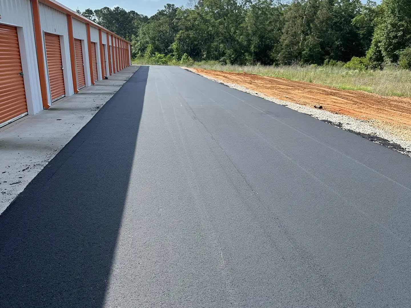 Fresh asphalt overlay on a lane beside a row of storage units, asphalt resurfacing
