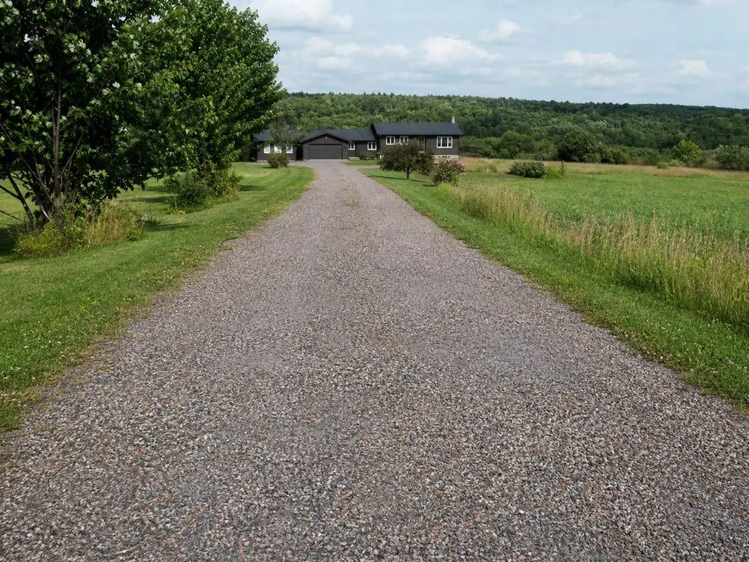 Chip seal lane running toward a house with fields on both sides, chip seal