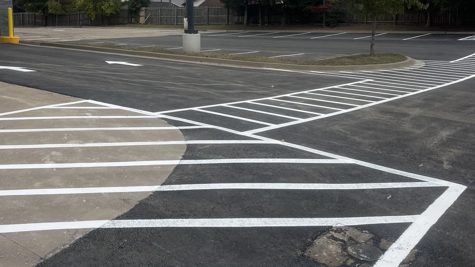 Hatched crosswalk and stall lines on a fresh parking lot under a light pole, parking lot striping
