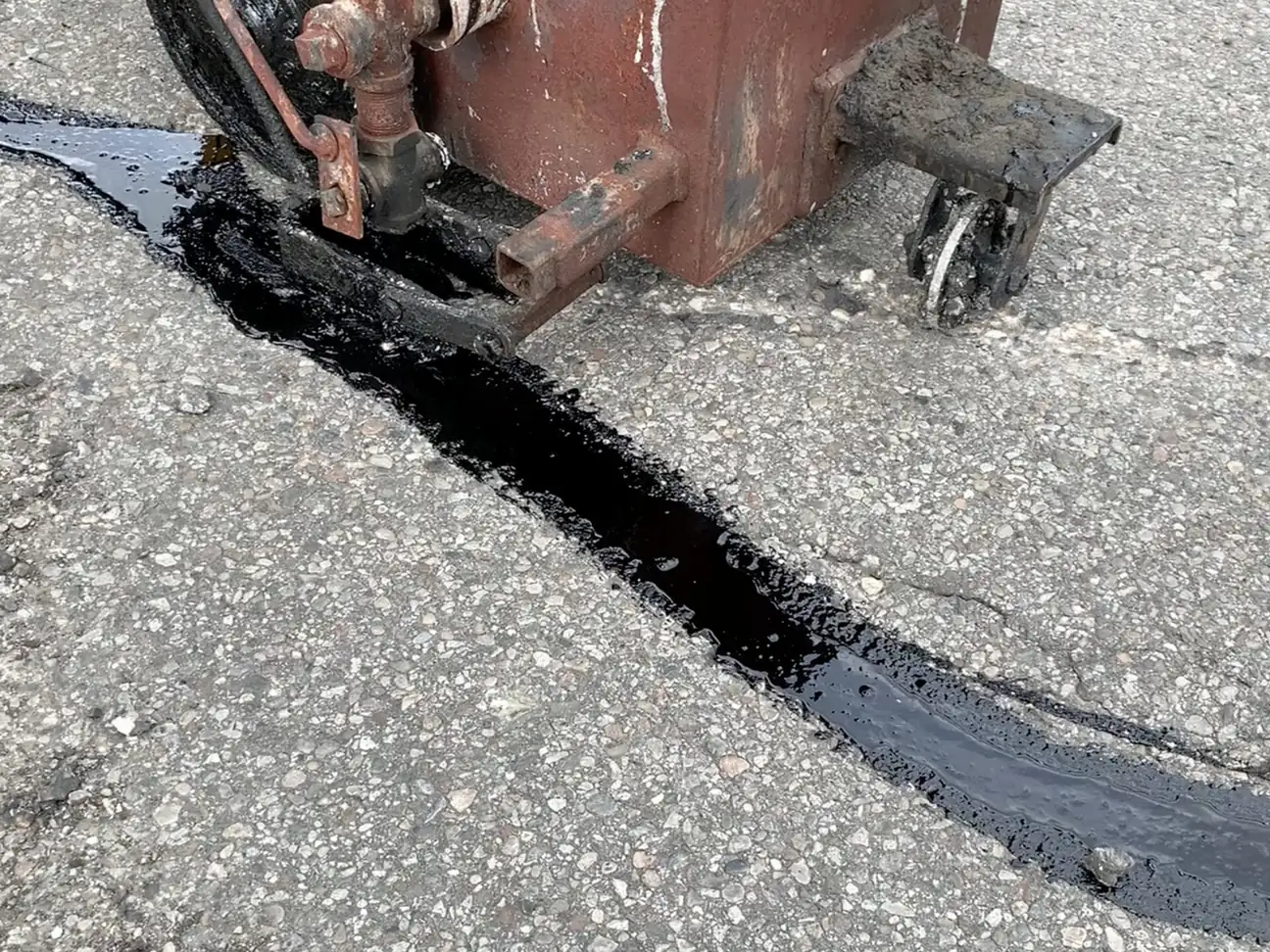 Hot pour crack sealer applied to a crack in asphalt, crack sealing