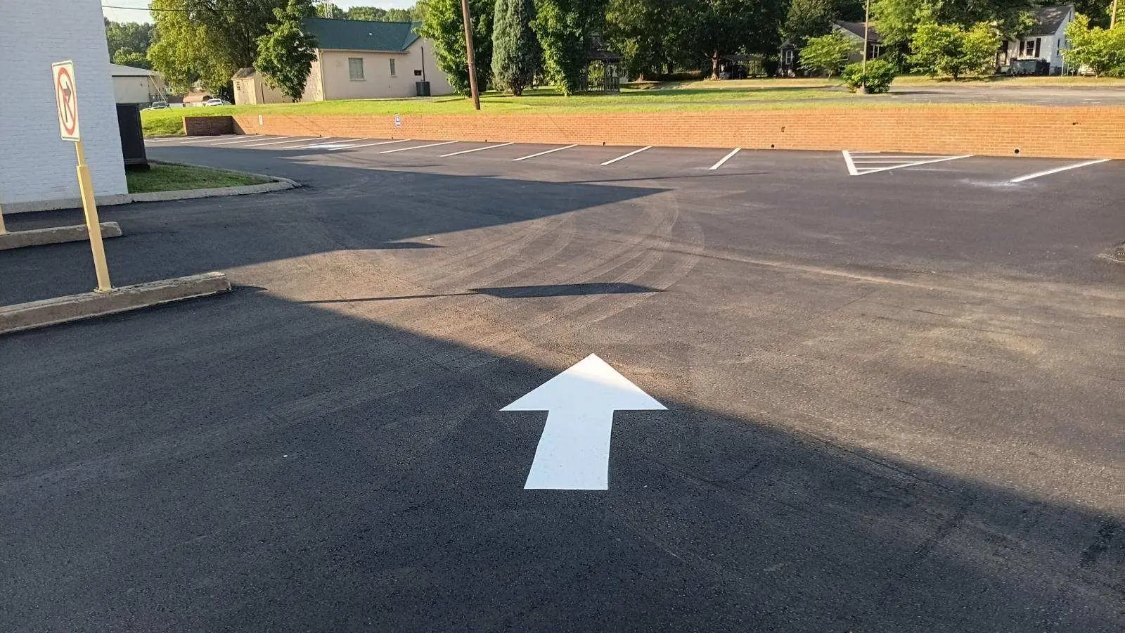 Directional arrow on fresh asphalt beside a brick wall, parking lot striping