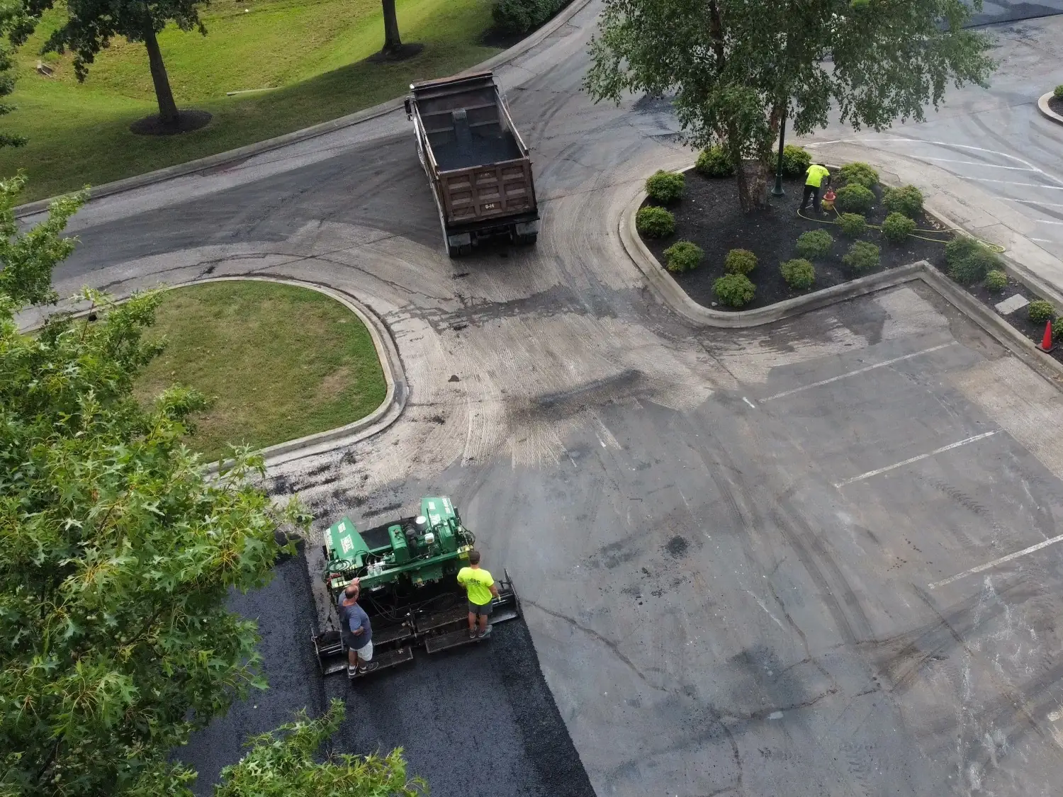 Paver and dump truck laying new asphalt at a shopping center lot entrance seen from above, parking lot paving