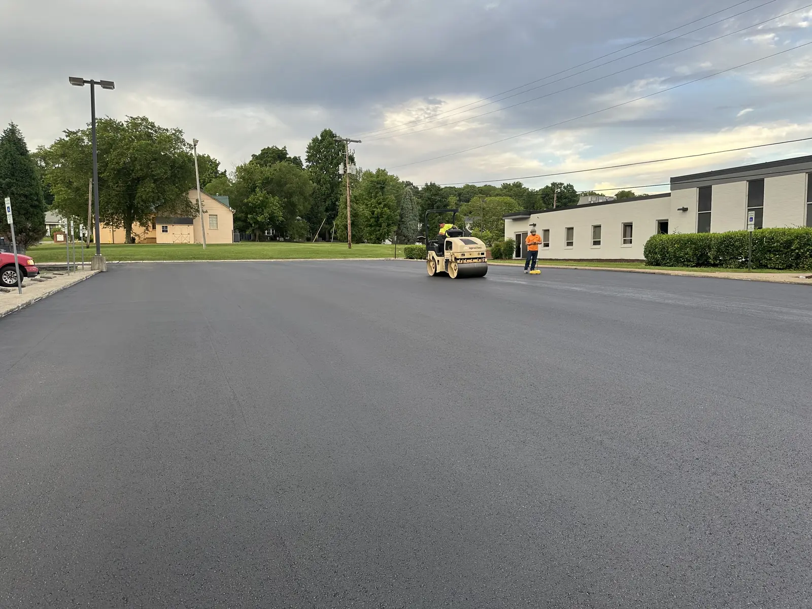 Roller compacting a freshly paved parking lot at dusk beside an office building, parking lot paving