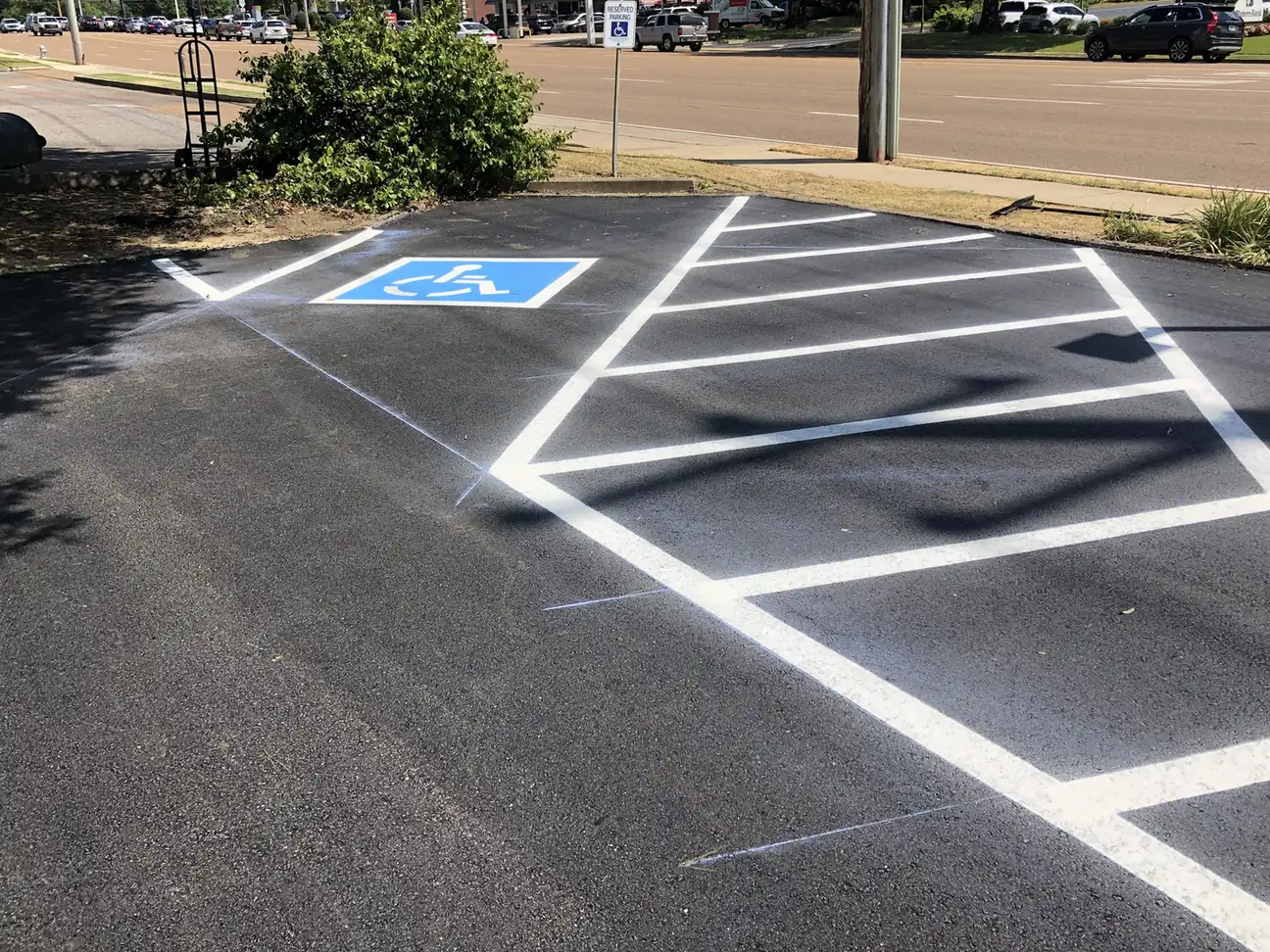 Accessible parking stall with blue symbol and white hatched aisle on fresh asphalt, parking lot striping