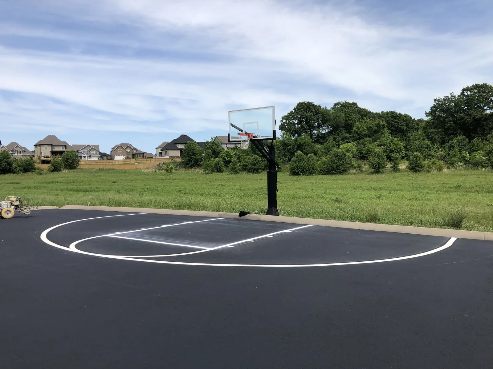 Basketball court lines painted on fresh asphalt beside a grass field, pavement marking and striping