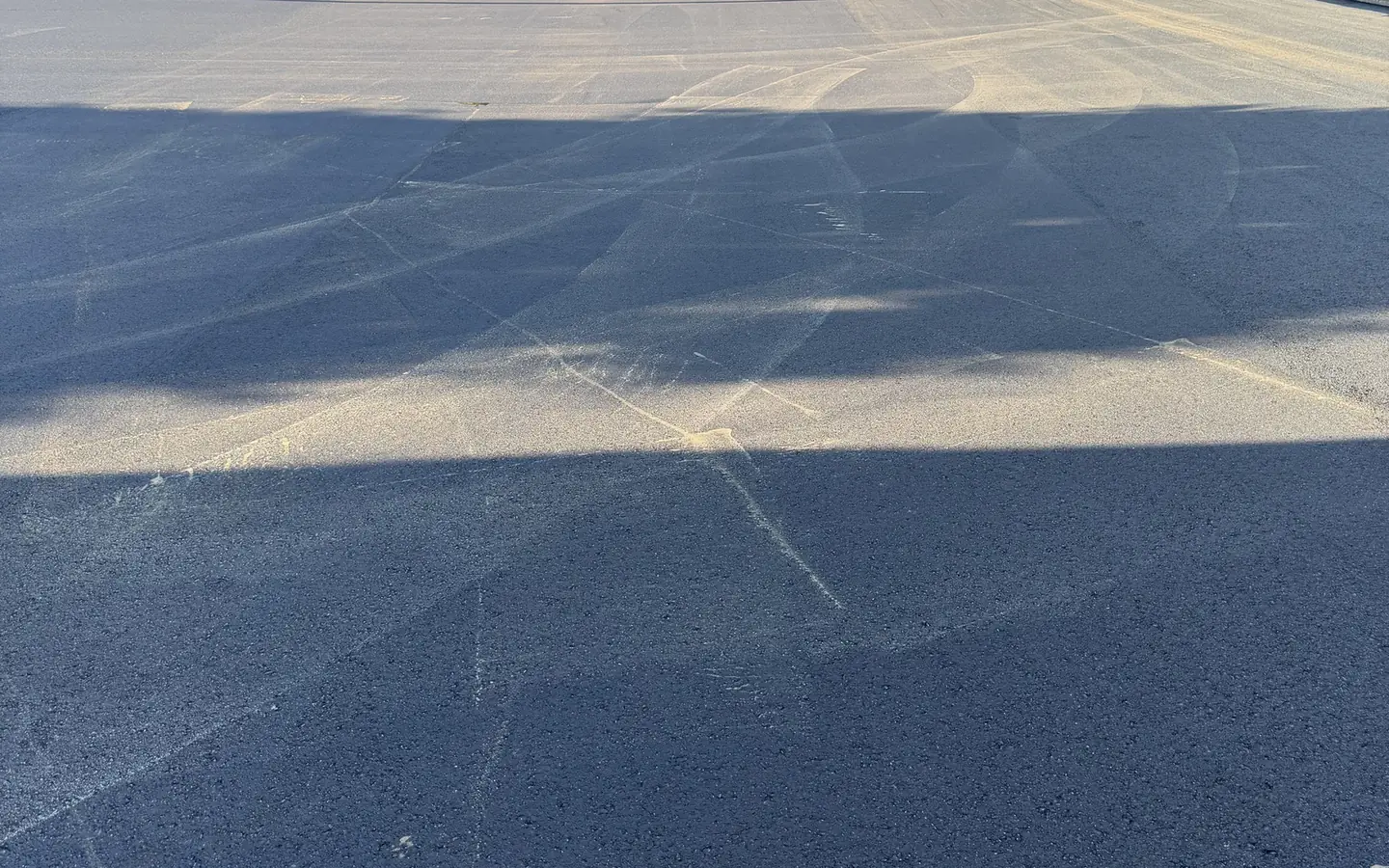 Freshly sealcoated parking lot drying beside a retaining wall and trees, parking lot sealcoating
