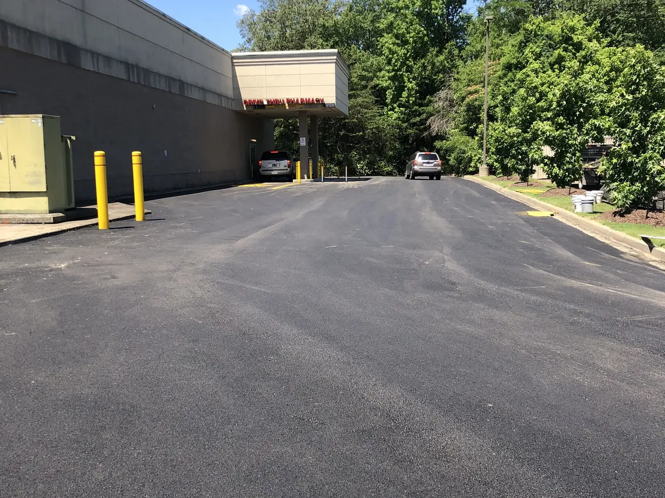 Sealcoated lane with a yellow bollard and shade trees, sealcoating