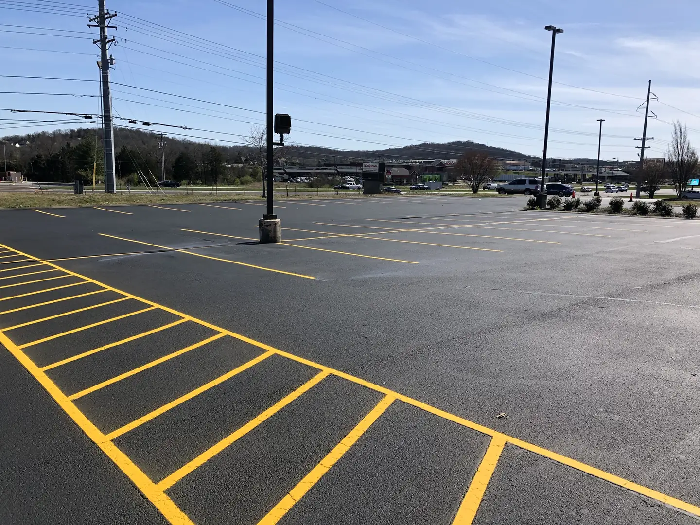 Freshly sealcoated lot with yellow stall lines and a light pole, sealcoating