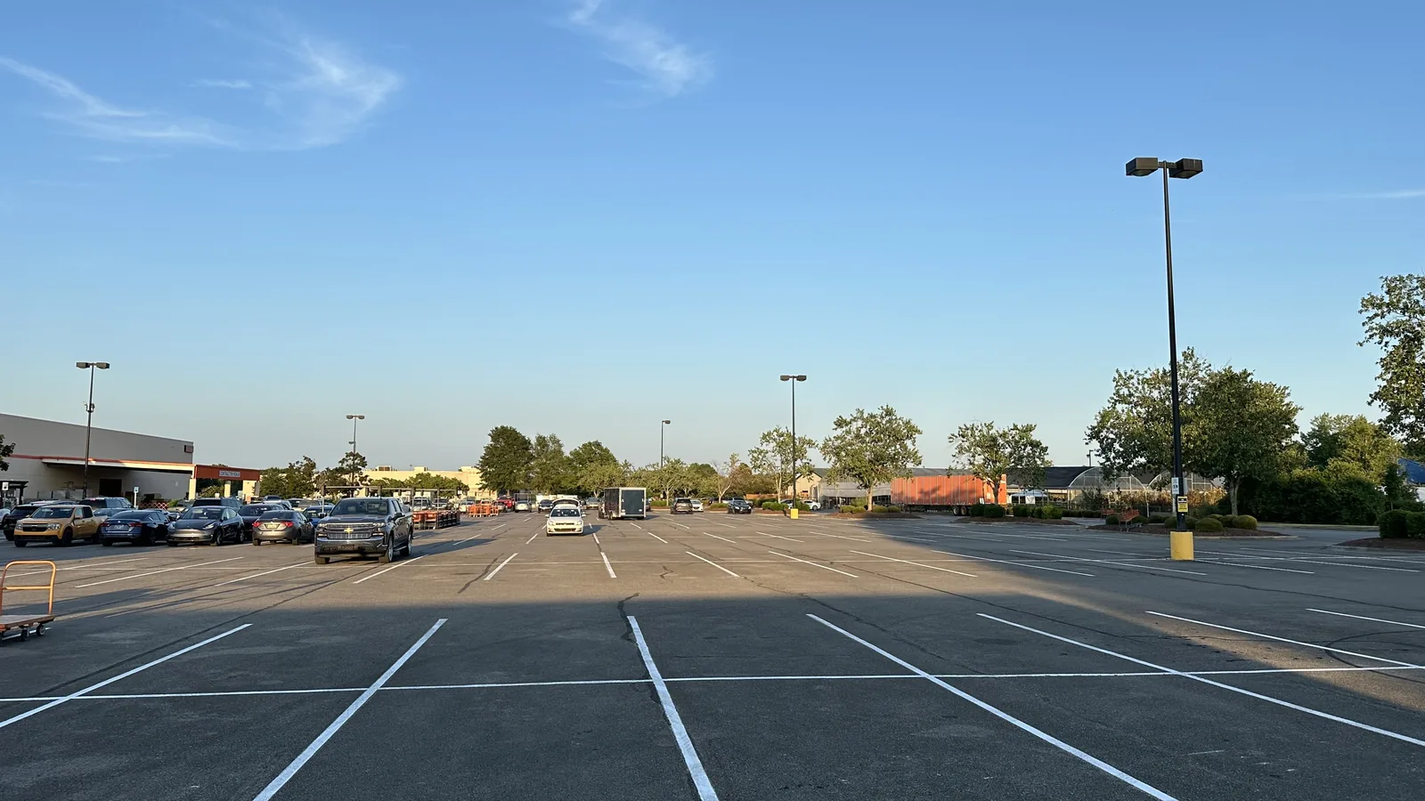 Freshly striped parking lot at dusk with light poles and trees, asphalt paving