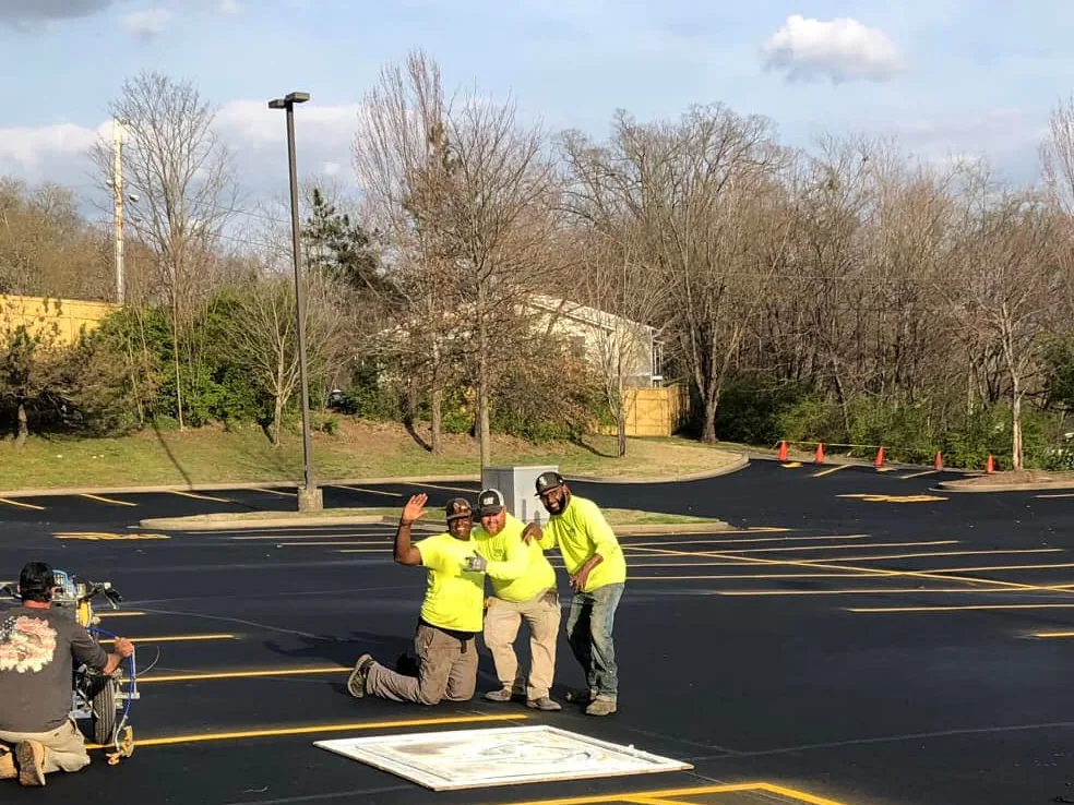 Three crew members in safety shirts on a freshly striped parking lot